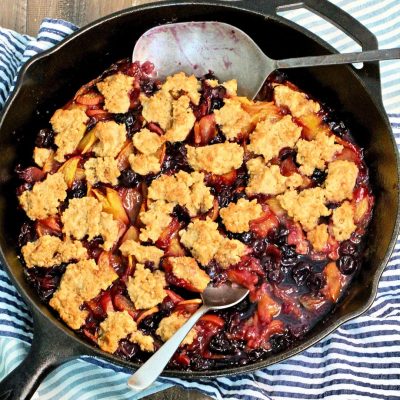 Freshly baked fruit cobbler with peaches and berries topped with golden crumble, served in a cast iron skillet on a rustic wooden table